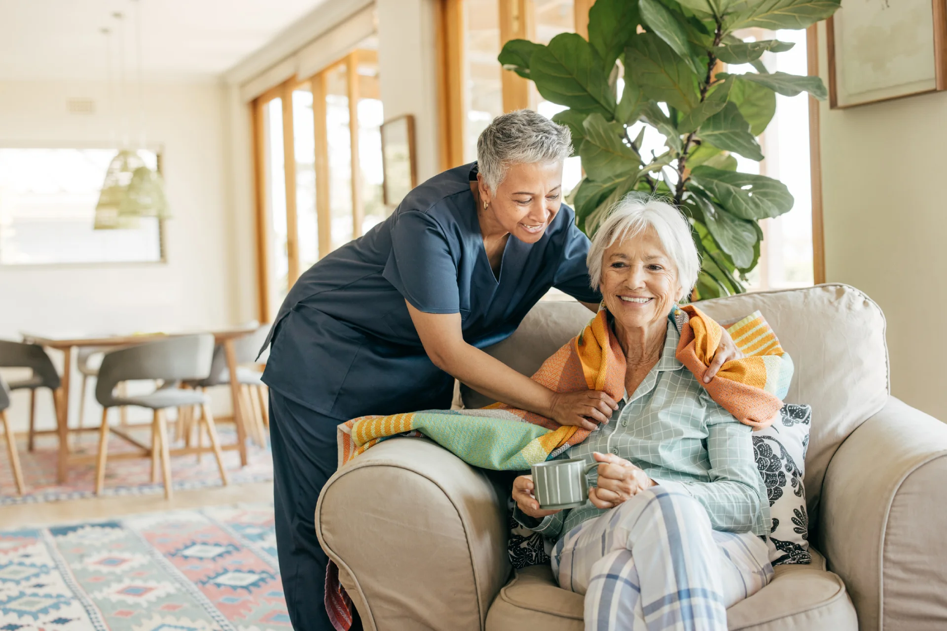 Loving caregiver wrapping happy senior in a warm blanket in Wasilla AK